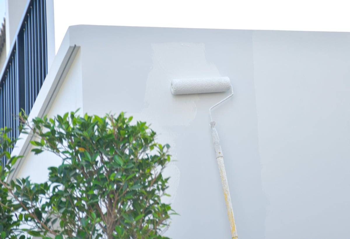 Worker painting the exterior wall of a house with a paint roller