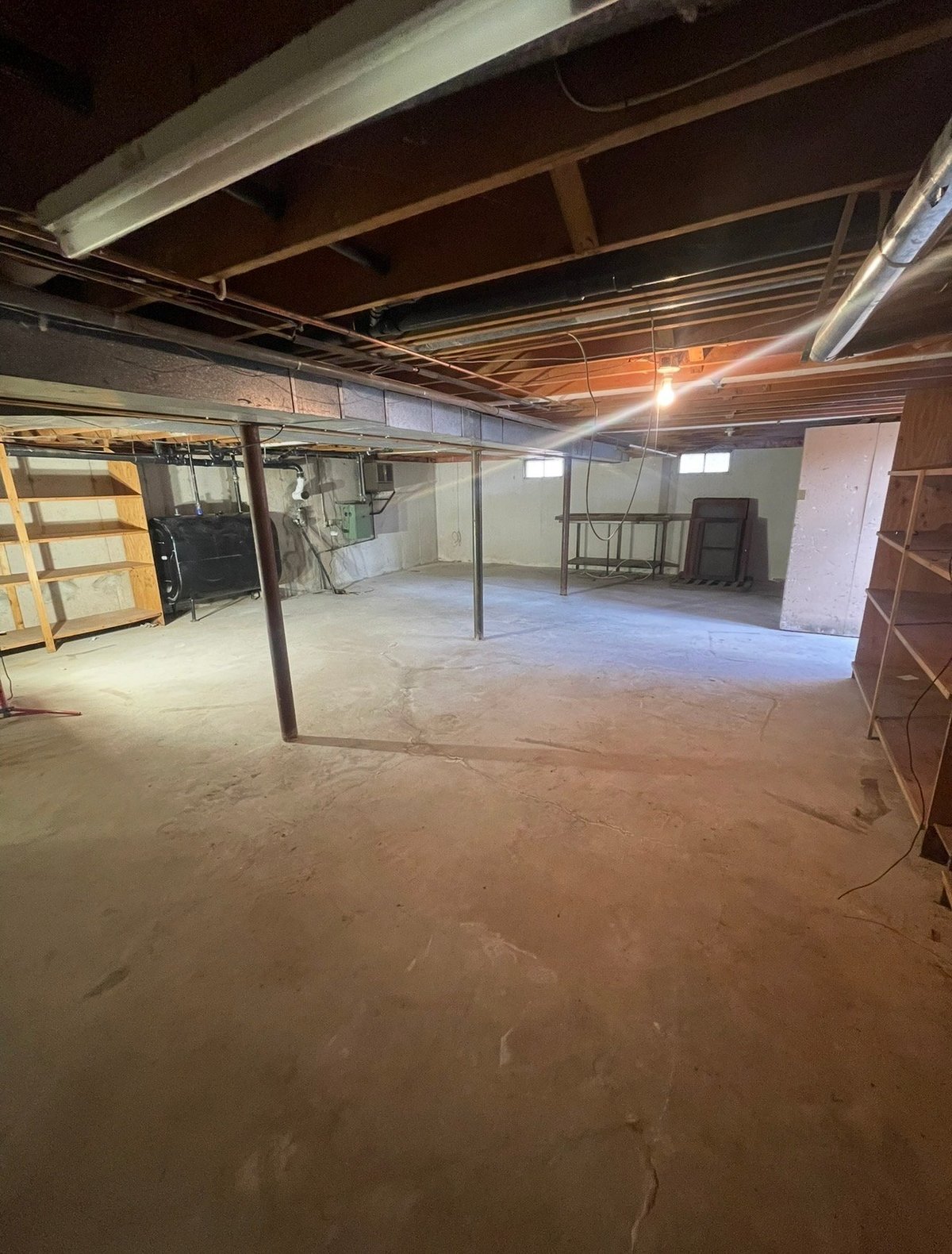 Empty unfinished basement with concrete floor, support columns, exposed wood ceiling beams, and glass partitions ready for renovation