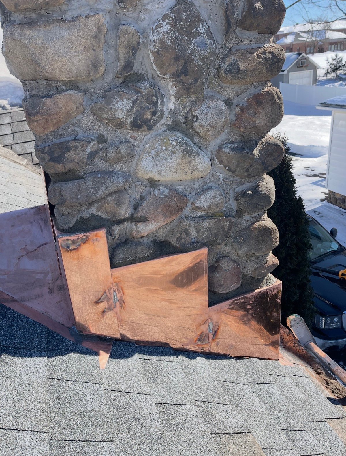 Large stacked stone chimney with wooden support base on a residential rooftop
