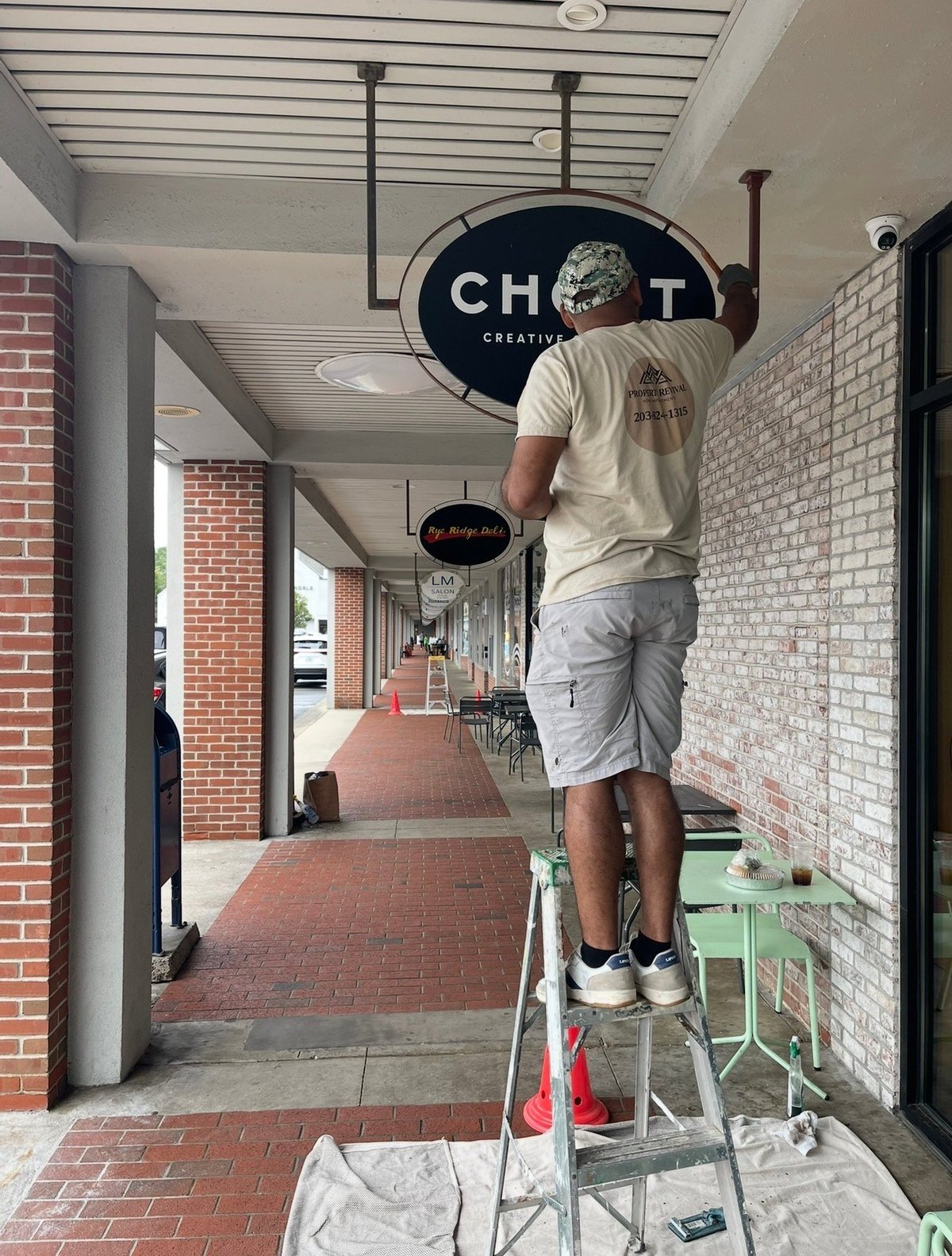 Man standing on ladder adjusting a CHVRT Creative sign hanging from ceiling in a brick hallway