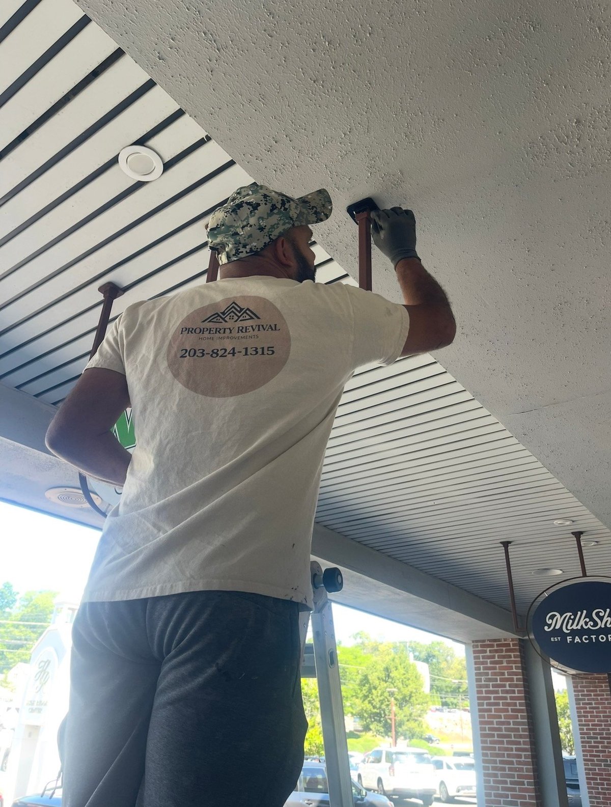 Worker in Property Revival shirt installing or adjusting ceiling fixture under striped white ceiling panels