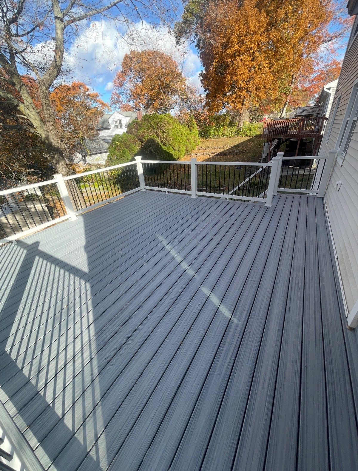 Gray composite deck with white railing overlooking autumn trees and neighborhood houses