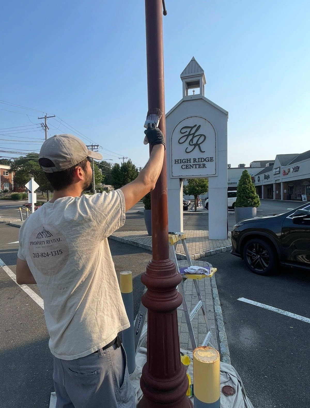 Man in white shirt and cap installing or adjusting a burgundy street lamp post with Beverly Ridge Center sign visible in background